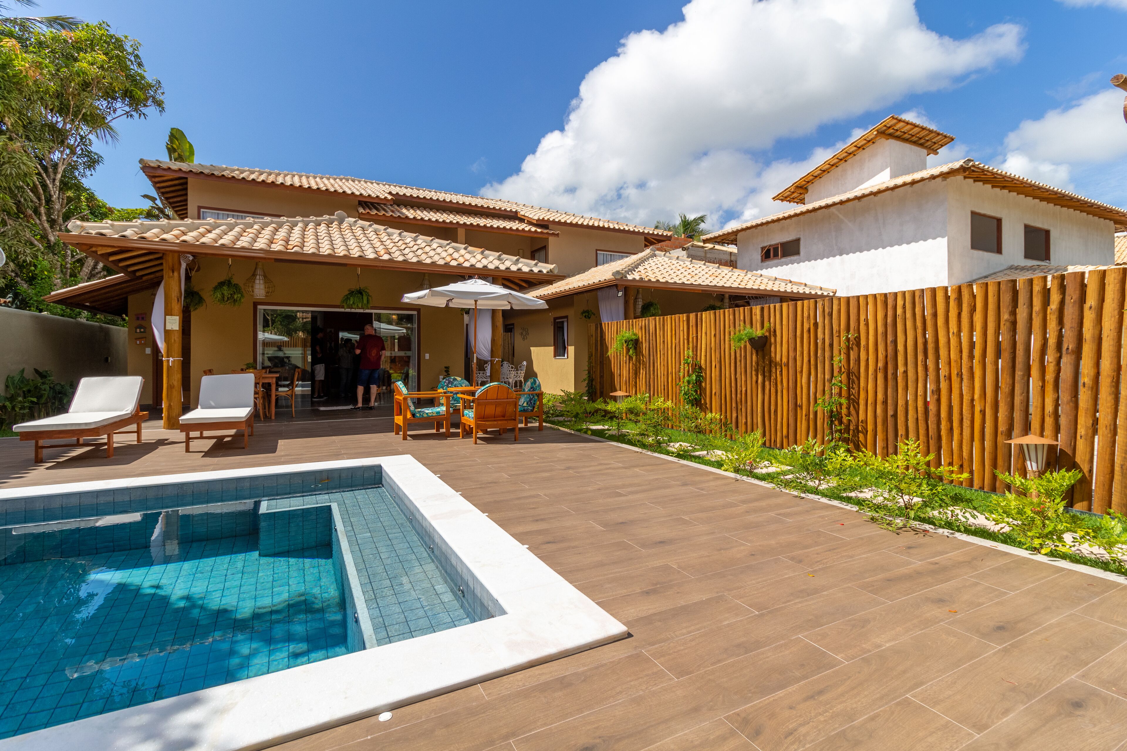 Uma área de piscina com um deck de madeira, cadeiras de descanso e uma pequena mesa com cadeiras.