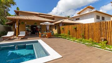 Uma área de piscina com um deck de madeira, cadeiras de descanso e uma pequena mesa com cadeiras.