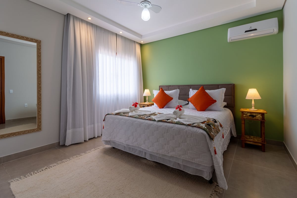 A neatly arranged hotel room with a large bed, two bedside tables with lamps, a mirror, and a ceiling fan.