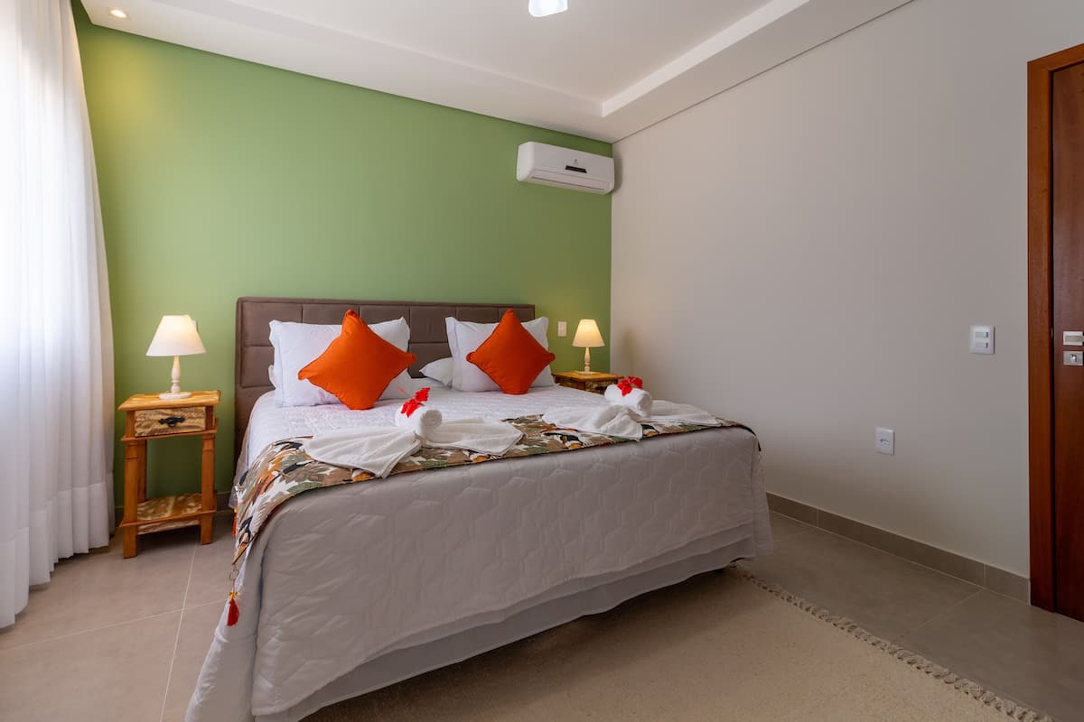 A neatly made bed with white and orange pillows, a patterned bedspread, and two bedside tables with lamps.