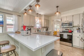 A modern kitchen with white cabinetry, a large island, stainless steel appliances, and pendant lighting. - Butterfly: Downtown Stay Near CMU (Grand Junction)