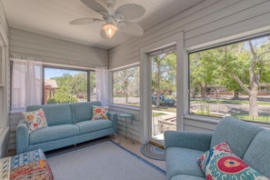 A sunroom with a blue sofa, a small table, and a ceiling fan. - Butterfly: Downtown Stay Near CMU (Grand Junction)