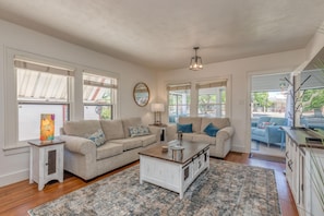 A spacious living room with two sofas, a coffee table, and a rug. There are large windows with blinds, a ceiling light, and a view of the outdoors. - Butterfly: Downtown Stay Near CMU (Grand Junction)