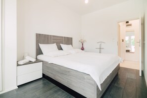 Une chambre moderne avec une tête de lit en bois, une literie blanche et une table de chevet sur laquelle se trouvent un téléphone et un vase.