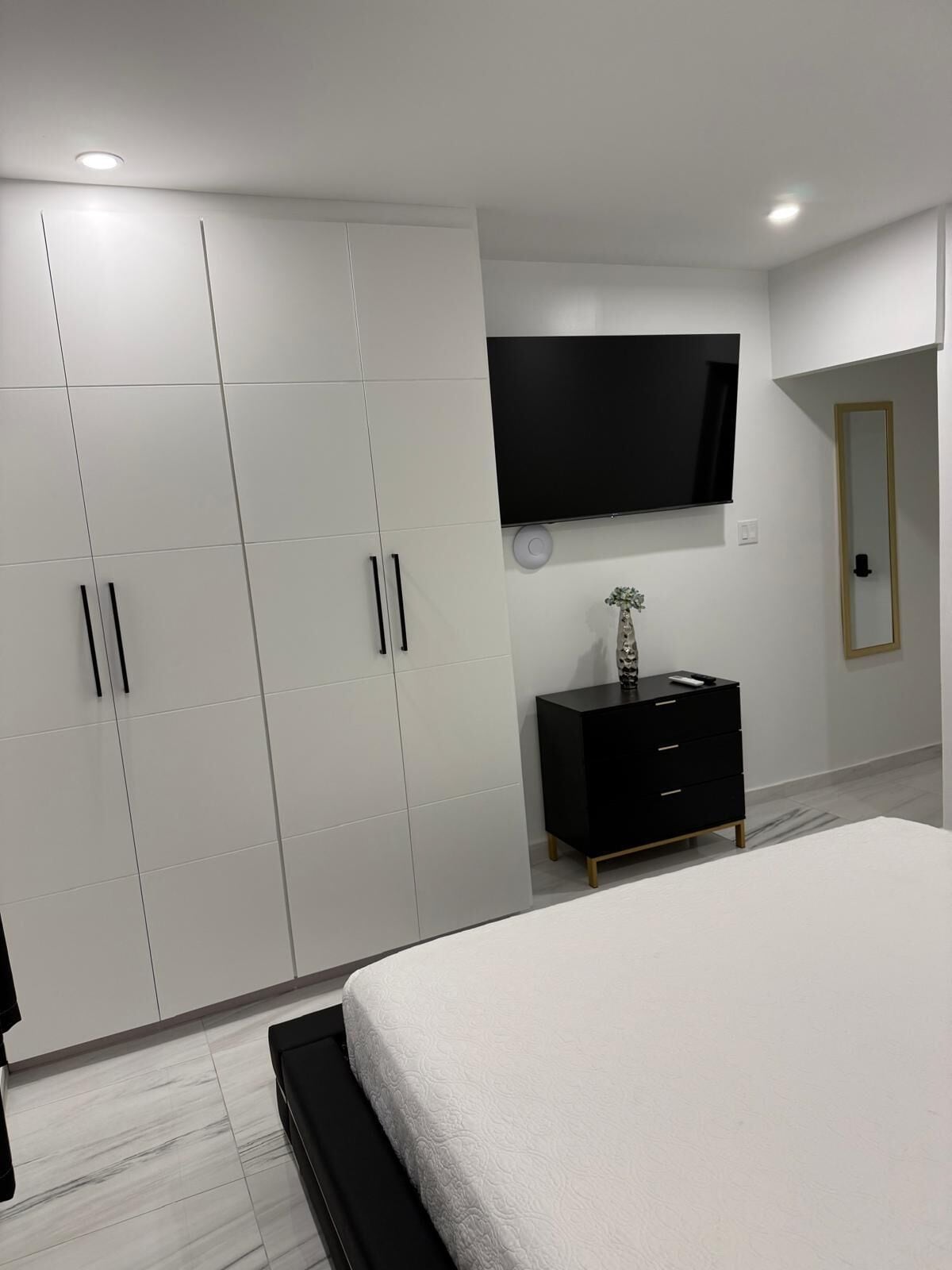 Ein modernes Schlafzimmer mit einem großen Bett, einem an der Wand montierten Fernseher und einem Schrank mit mehreren Türen.