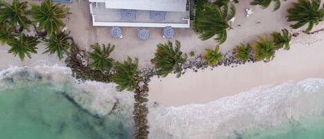 An aerial view of a beachside property with a large house, a boat, and several palm trees.