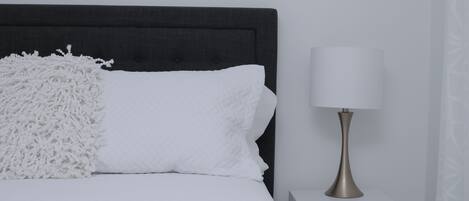 Een net opgemaakt bed met witte beddengoed en een zachte witte plaid, een bedlampje en een witte nachtkastje.
