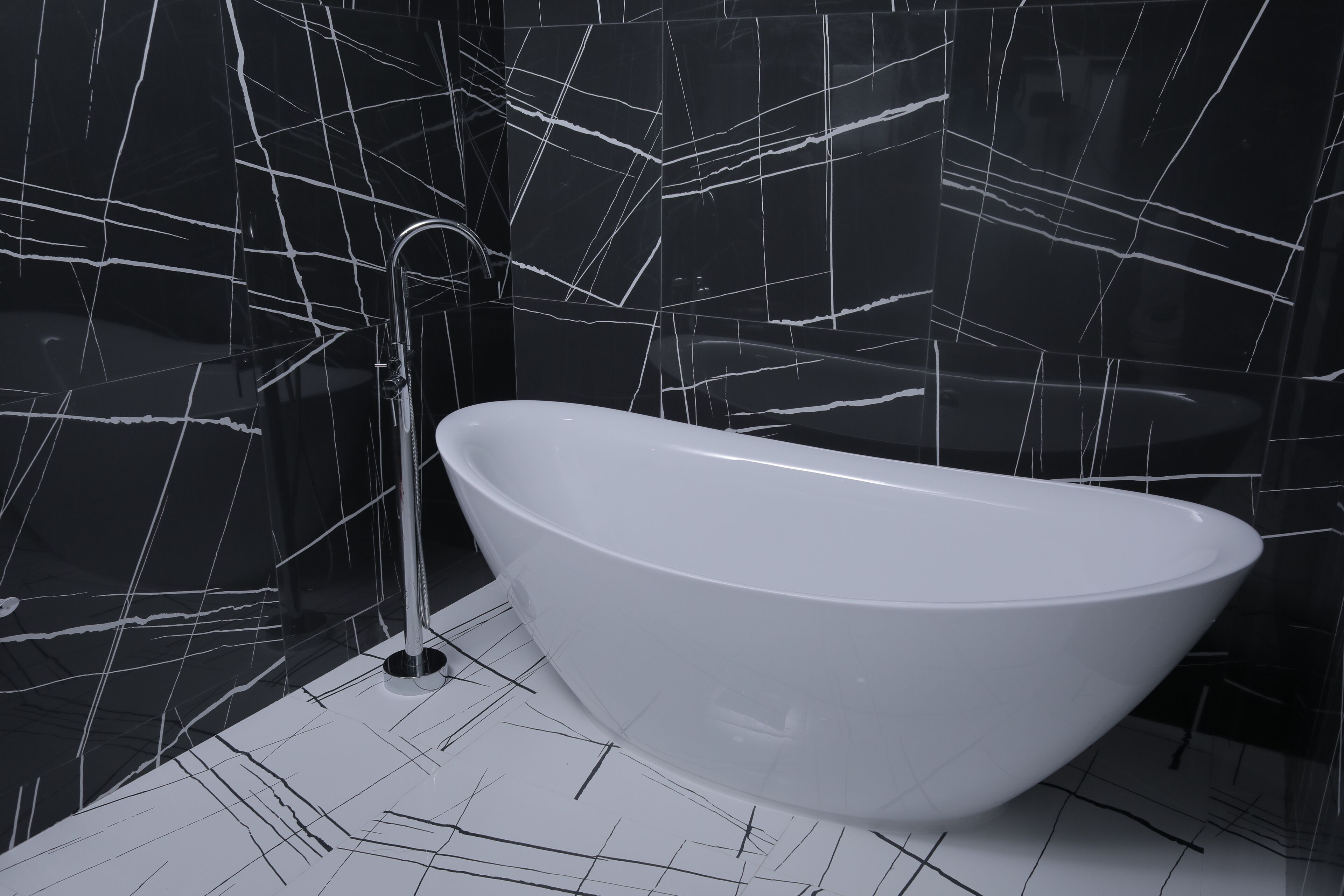 A modern bathroom with a freestanding bathtub, black marble walls with white veining, and a white tiled floor.