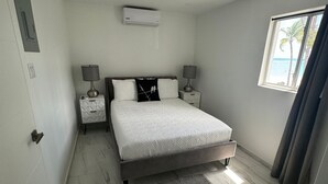 Un dormitorio moderno con una cama grande, dos mesitas de noche con lámparas, una alfombra pequeña y una ventana con vistas a la playa.