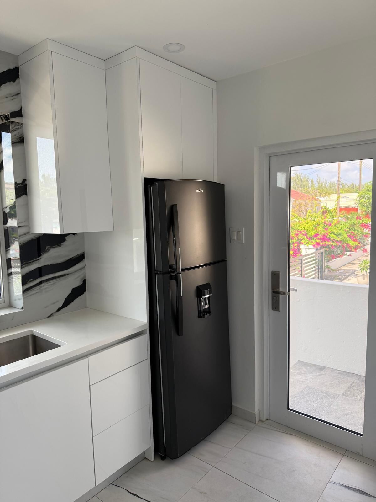 Eine moderne Küche mit weißen Schränken, einem schwarzen Kühlschrank und einem Fenster mit Blick auf einen Garten.