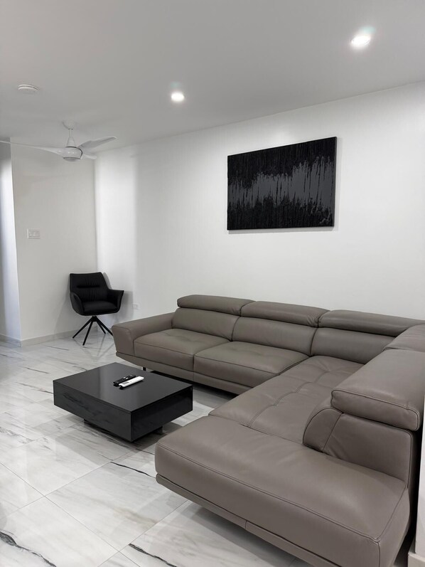 A modern living room with a sectional sofa, a black coffee table, a black armchair, and a large abstract painting on the wall. - The Royal Bliss Barbados (Worthing)