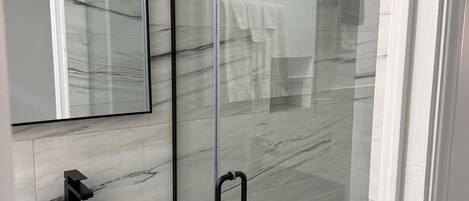 Un baño moderno con cabina de ducha de vidrio, lavamanos de mármol negro y un espejo grande.