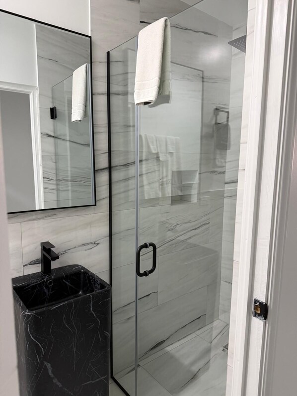 Un baño moderno con cabina de ducha de vidrio, lavamanos de mármol negro y un espejo grande.