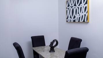 A minimalist room with a table and four chairs, a black abstract painting on the wall, and a sculptural object on the table.