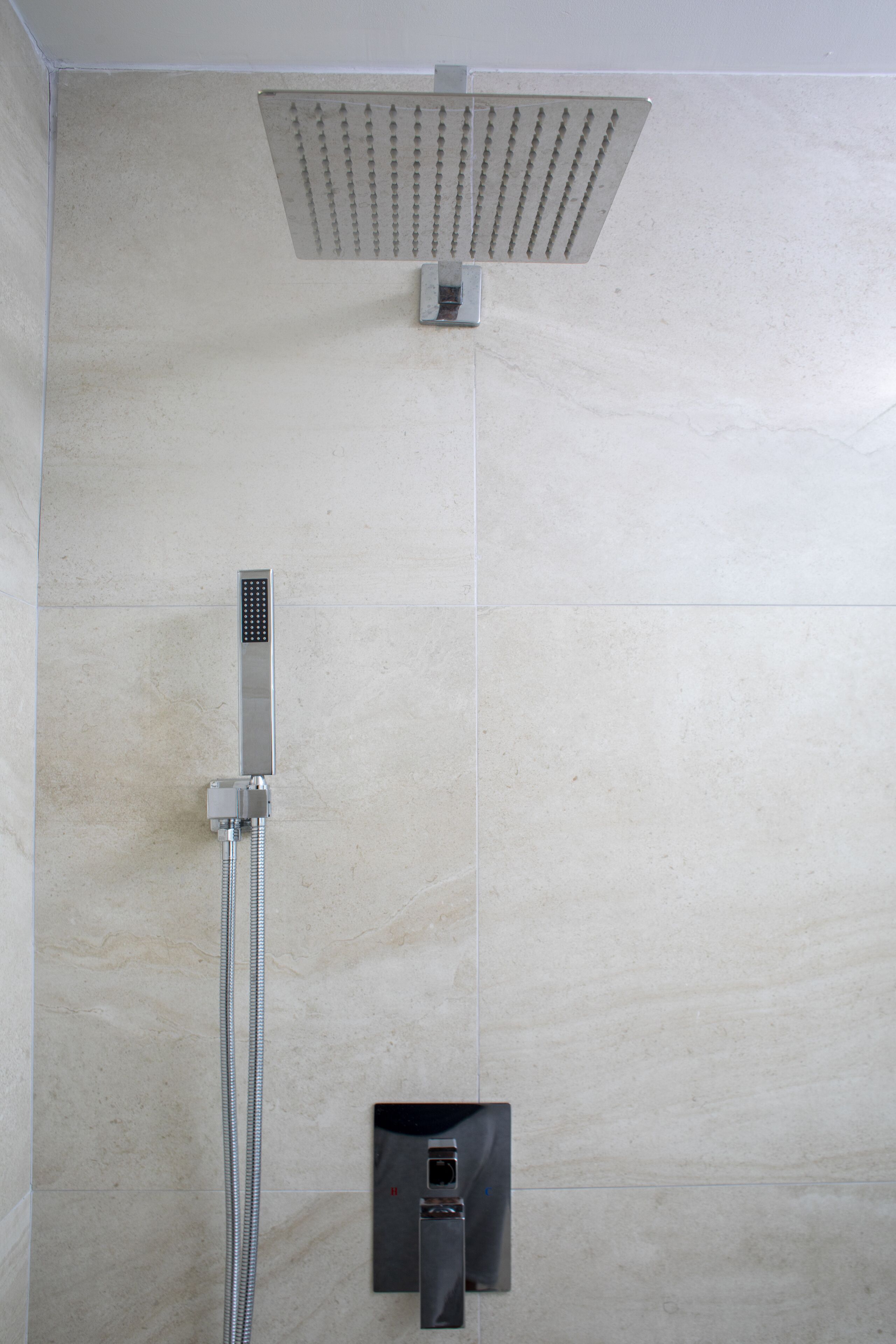 A shower with a square overhead head and a vertical hose.