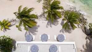 An aerial view of a beach with palm trees and a row of beach umbrellas. - The Royal Bliss Barbados (Worthing)