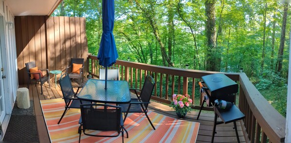 A wooden deck with a table and chairs, a grill, and a potted plant with pink flowers. - Back of the 9 - Charming townhome w/ lake views (Hot Springs)