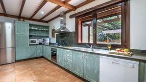 A kitchen with teal cabinets, a stainless steel refrigerator, a microwave, an oven, and a dishwasher. There is a window with a view of greenery outside. - Montion Jimera de Libar by Ruralidays (Málaga)