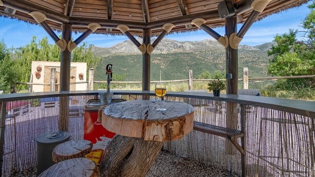 An outdoor seating area with a round wooden table, a red cooler, and a glass of wine. - Montion Jimera de Libar by Ruralidays (Málaga)
