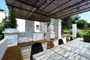 Eine Terrasse im Freien mit Tisch und Stühlen, einem überdachten Pergola und einem Garten im Hintergrund.