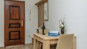 Una habitación con puerta de madera, un espejo, una mesa con una silla, un florero con flores y una botella.
