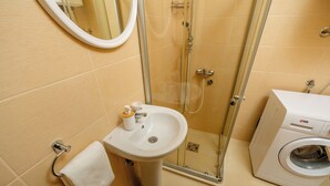 Un baño con lavamanos, espejo, ducha y lavadora.