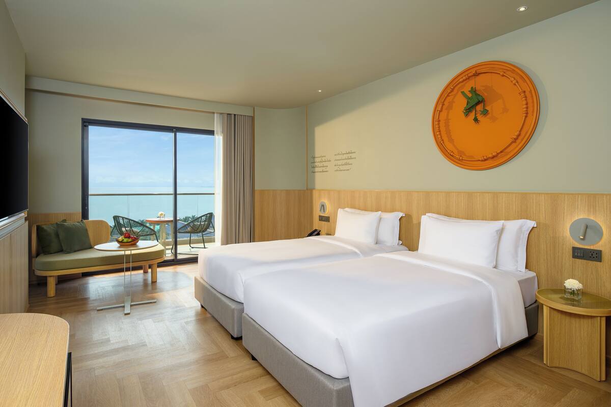 A hotel room with two beds, a sofa, a small table, and a balcony with a view.