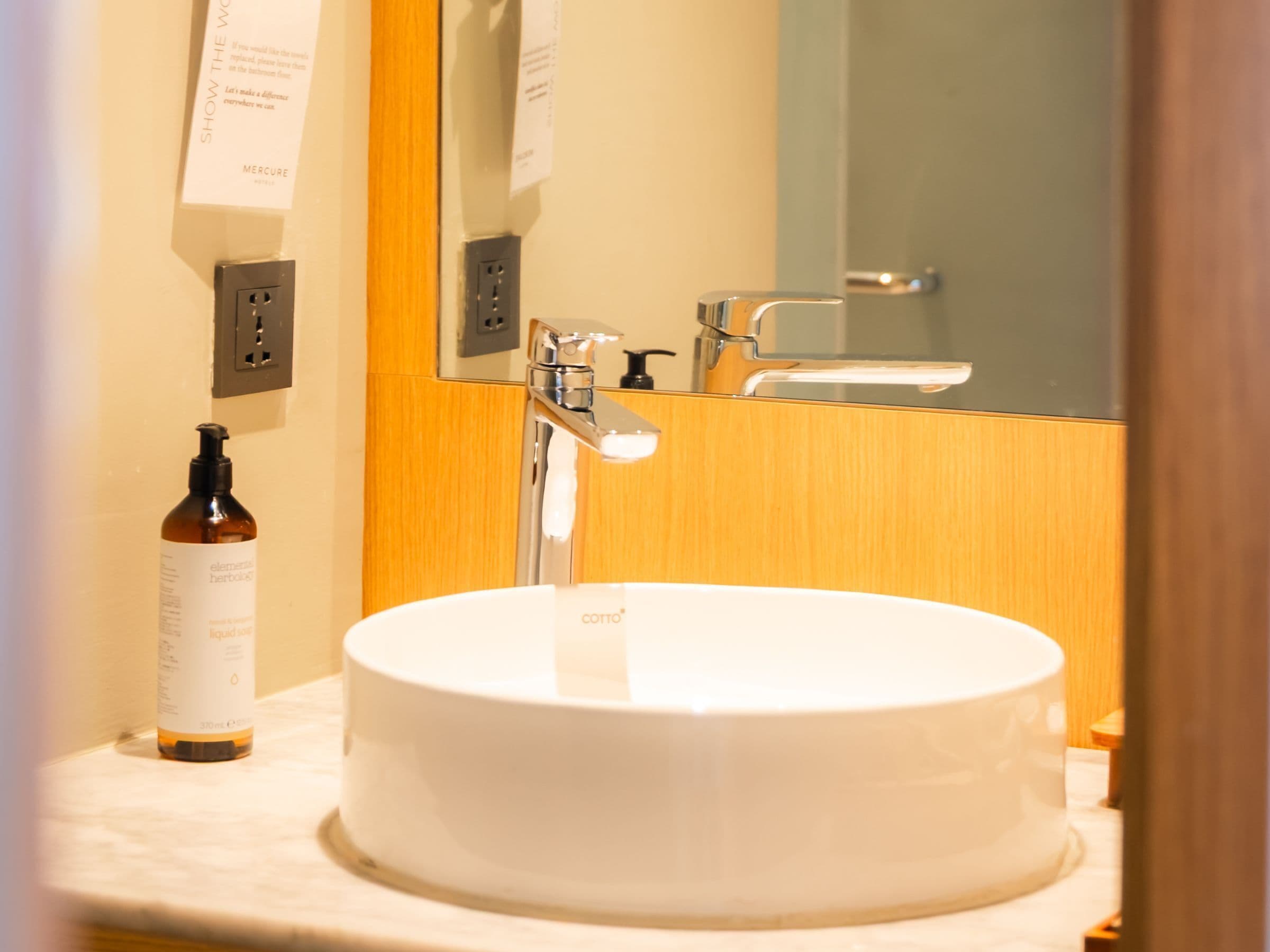A bathroom with a white sink, a mirror, a wooden vanity, and a bottle of Element Herbals.