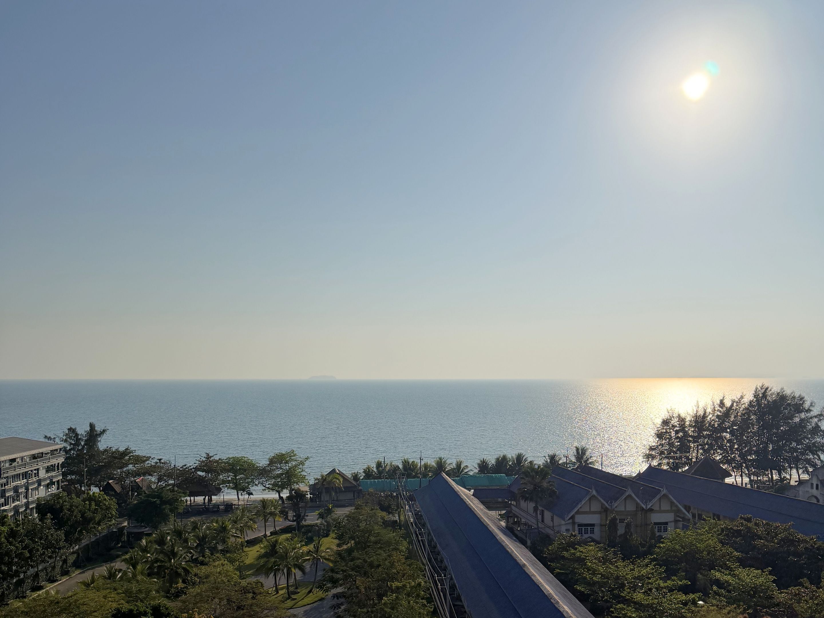 A coastal view with a clear sky, a body of water, and buildings with a sloped roof.