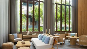 Un moderno salón con un sofá, sillas, una mesa de centro y amplios ventanales que dan a vistas de vegetación.