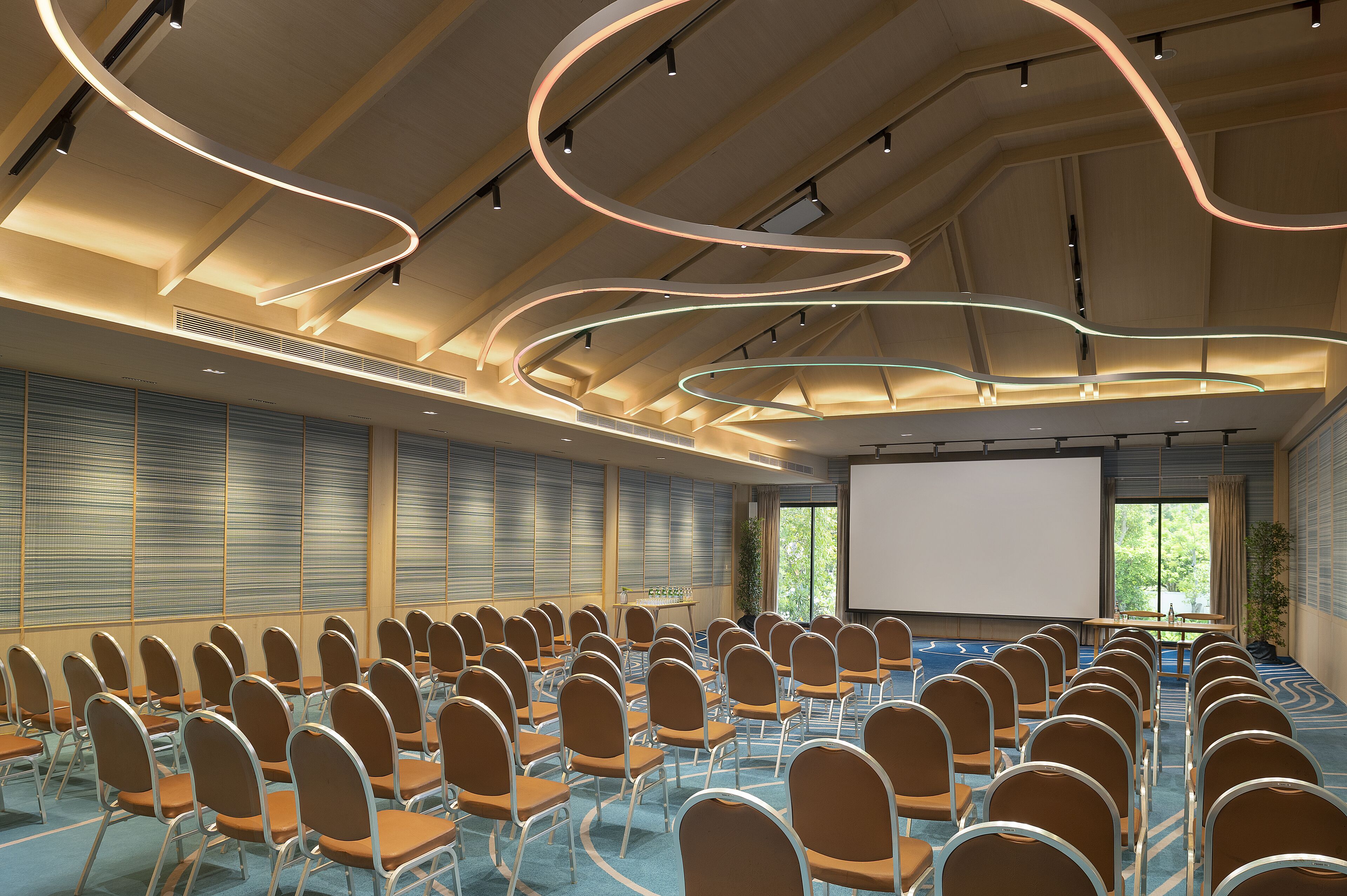 A conference room with rows of chairs, a projector screen, and a large window with blinds.