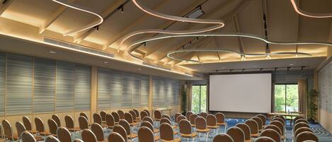 A conference room with rows of chairs, a projector screen, and a large window with blinds.