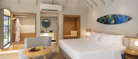 A modern hotel room with a large bed, a round dining table, a seating area, and a large mirror.