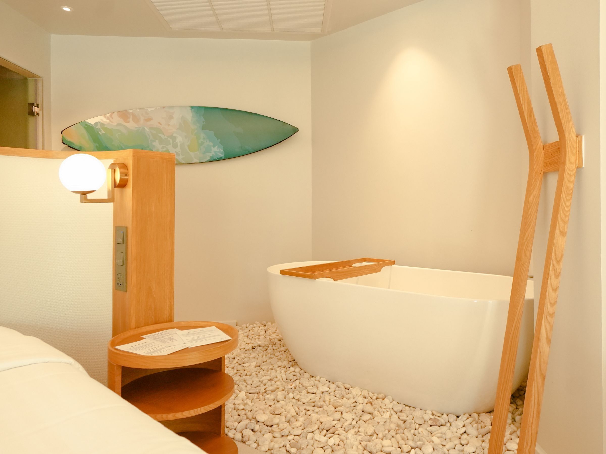A modern bathroom with a bathtub, a wooden shelf with papers, and a wall-mounted surfboard.