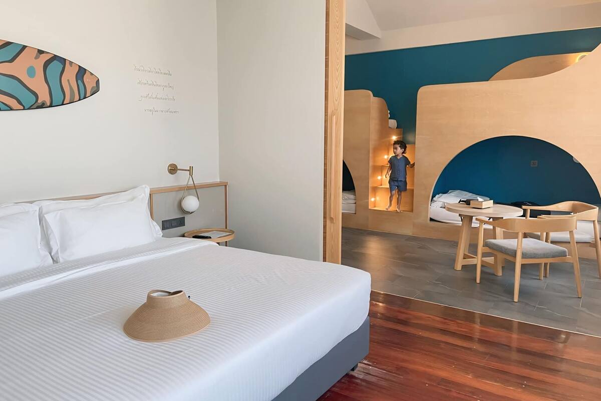 A modern hotel room with a large bed, a small desk, and a cozy seating area with a blue wall and wooden furniture.