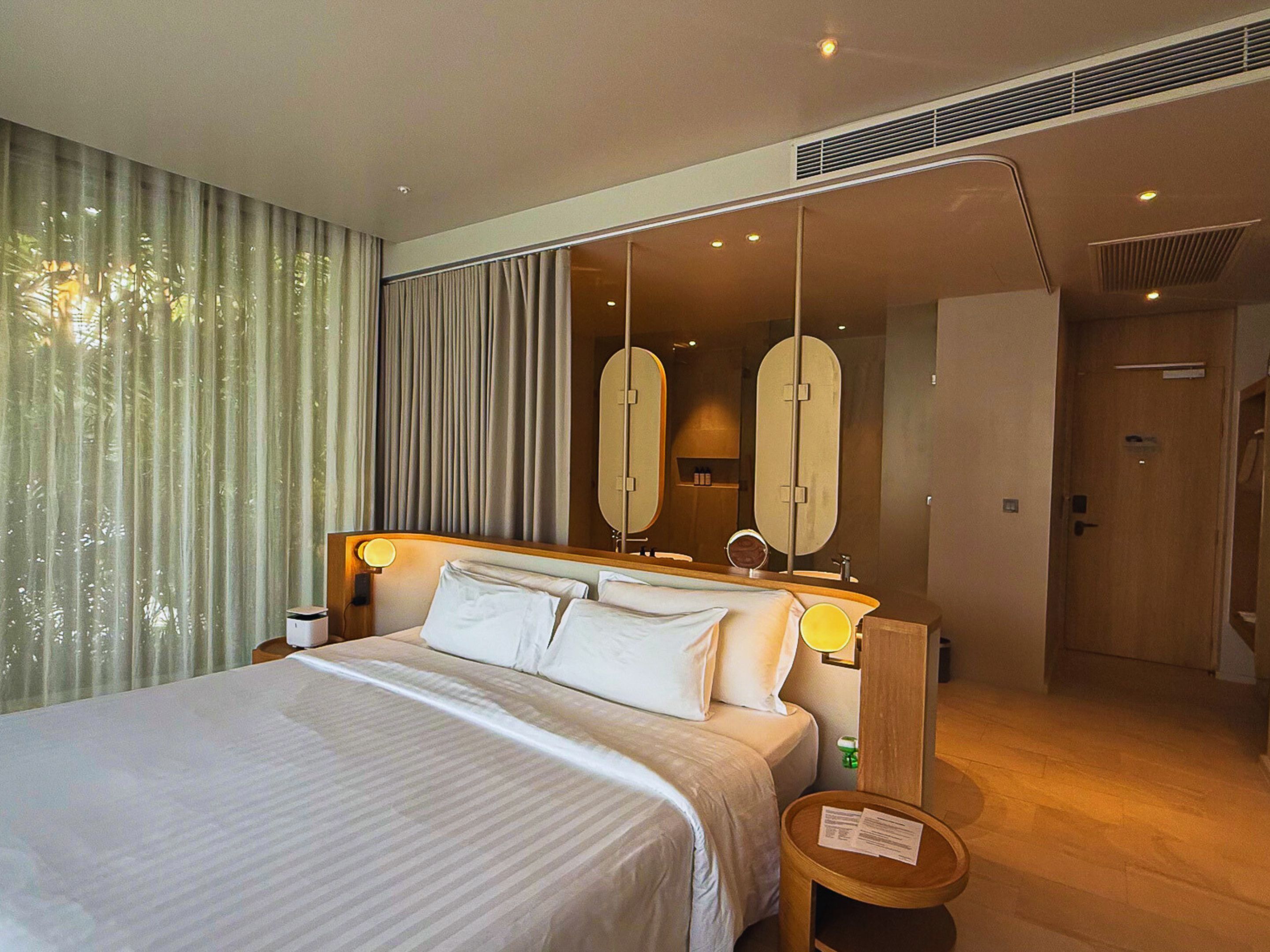 A hotel room with a large bed, a bedside table, a mirror, and a door leading to another room.
