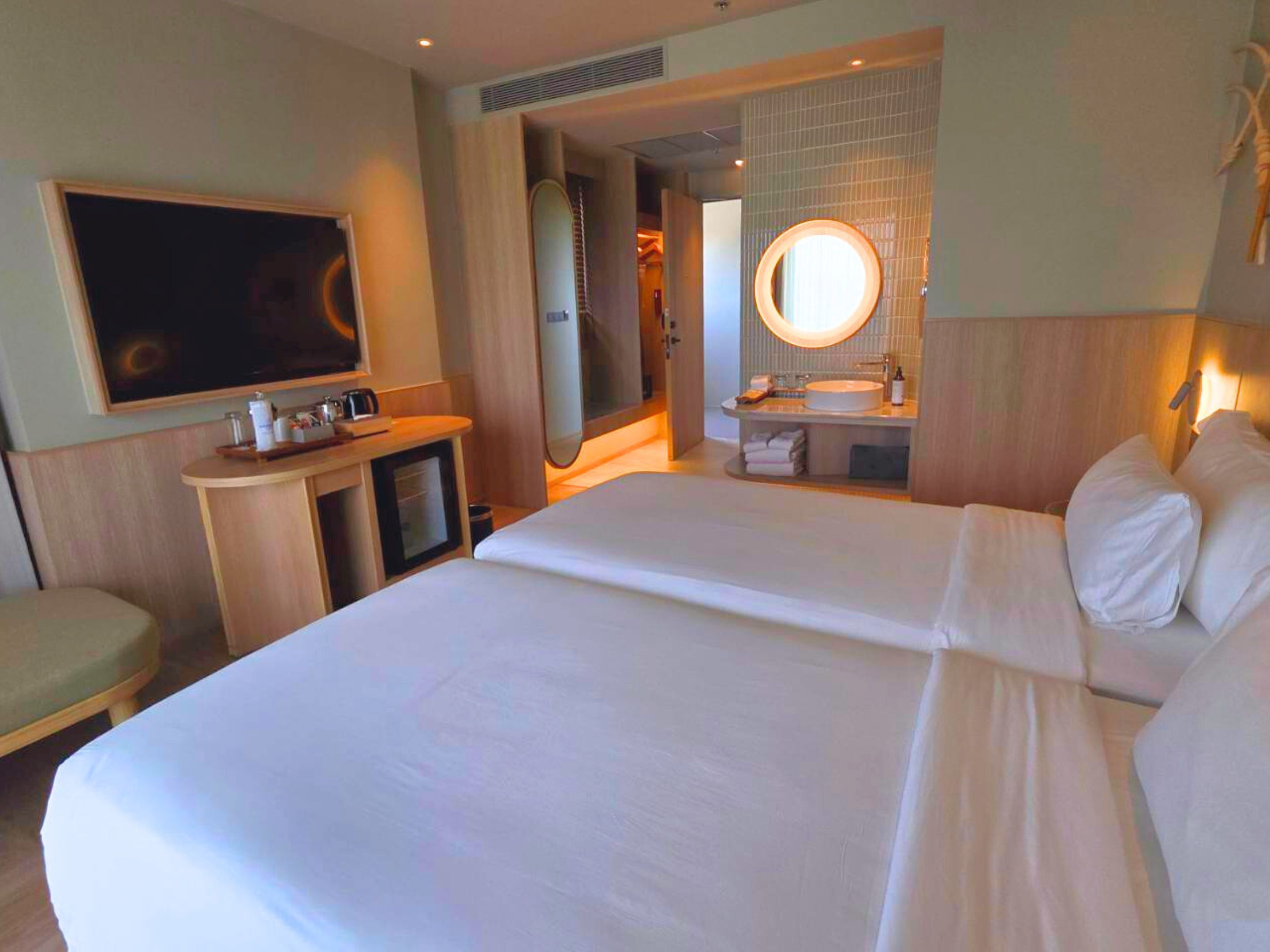 A hotel room with a large bed, a desk with a chair, a TV, a bathroom with a mirror, and a sink.