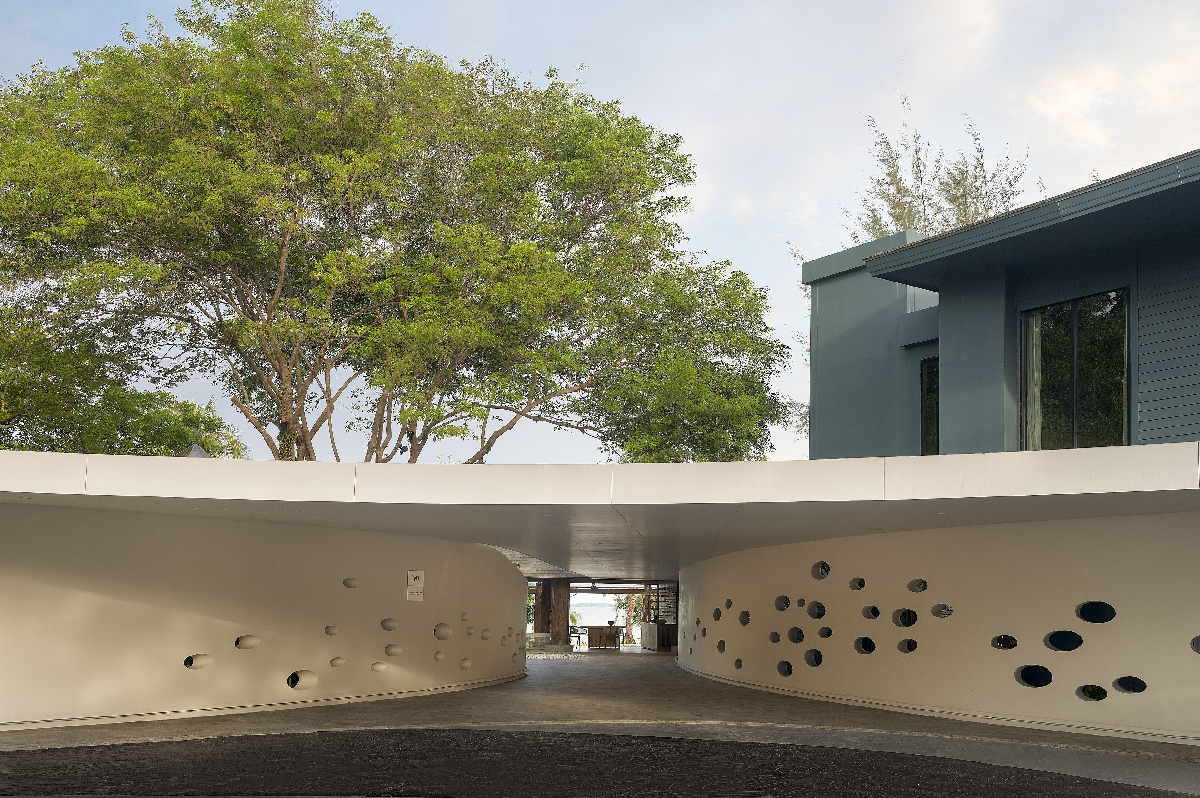 Un bâtiment moderne à la façade incurvée, ornée d’ouvertures circulaires, avec un arbre en arrière-plan et un ciel dégagé.