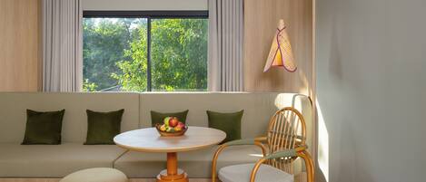 A modern living room with a sofa, a round table with a fruit bowl, a wooden chair, and a hanging lamp.