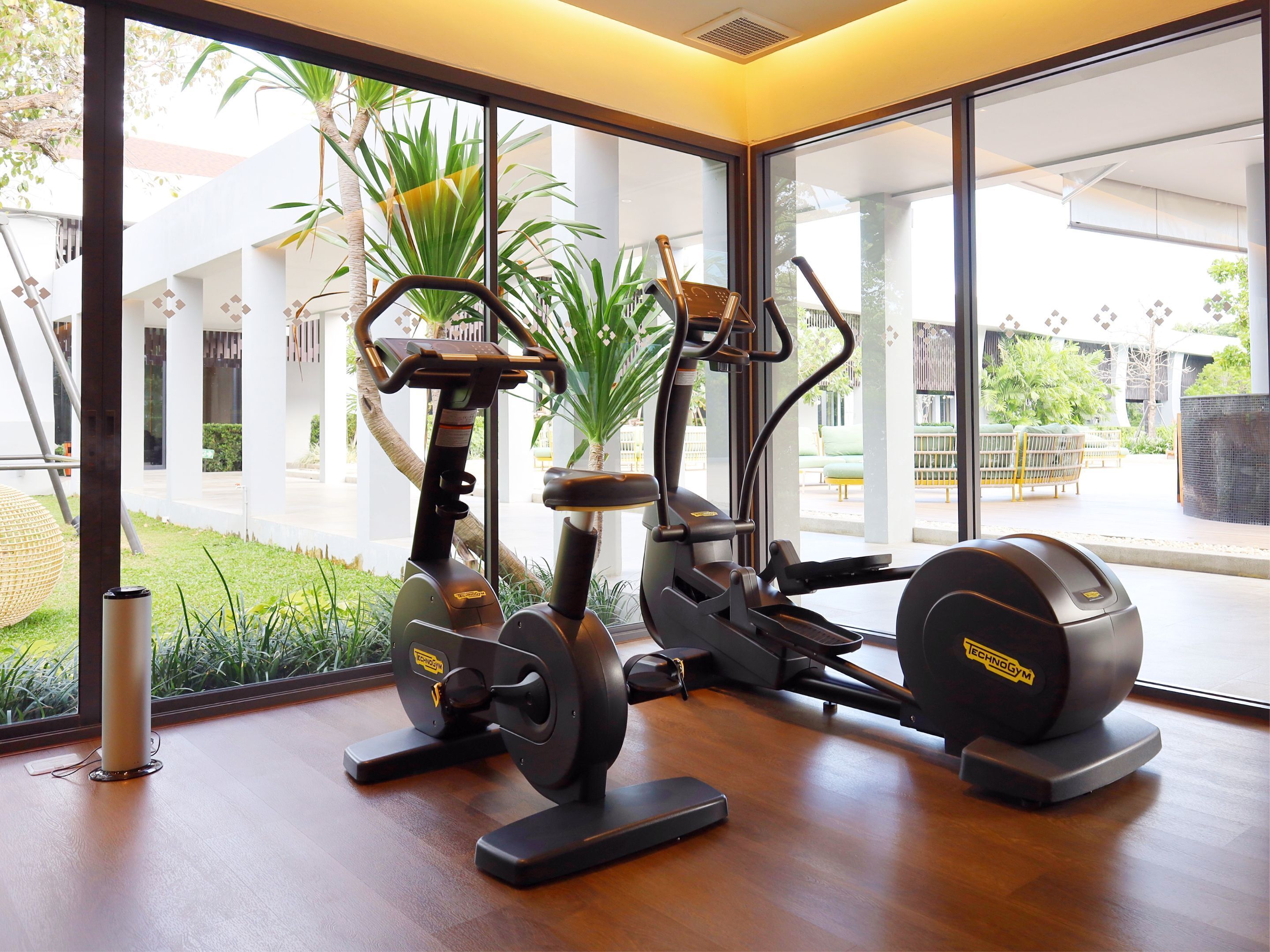 A gym with cardio machines and a kettlebell, large windows with a view of a courtyard.