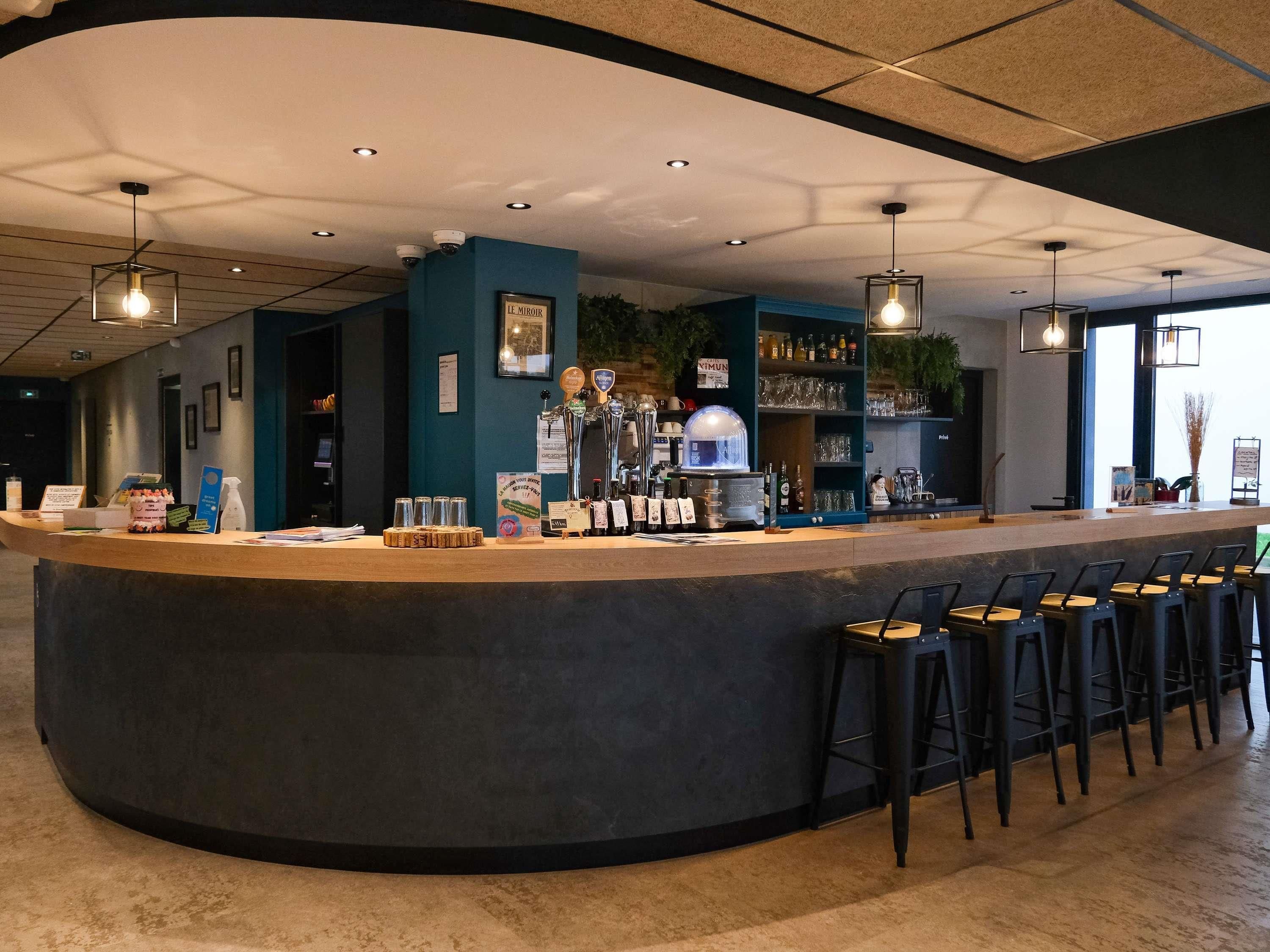 Zona de bar con mostrador curvo, varios taburetes y una amplia variedad de botellas y vasos.
