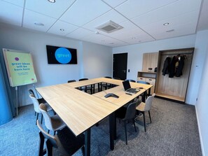 Une salle de conférence avec une longue table, des chaises, un tableau blanc et un panneau indiquant « Bienvenue » sur le mur.