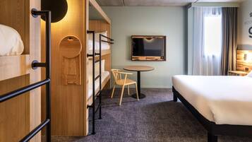 Una habitación de hotel con una cama litera, una cama individual, un televisor, una mesita pequeña y una silla.