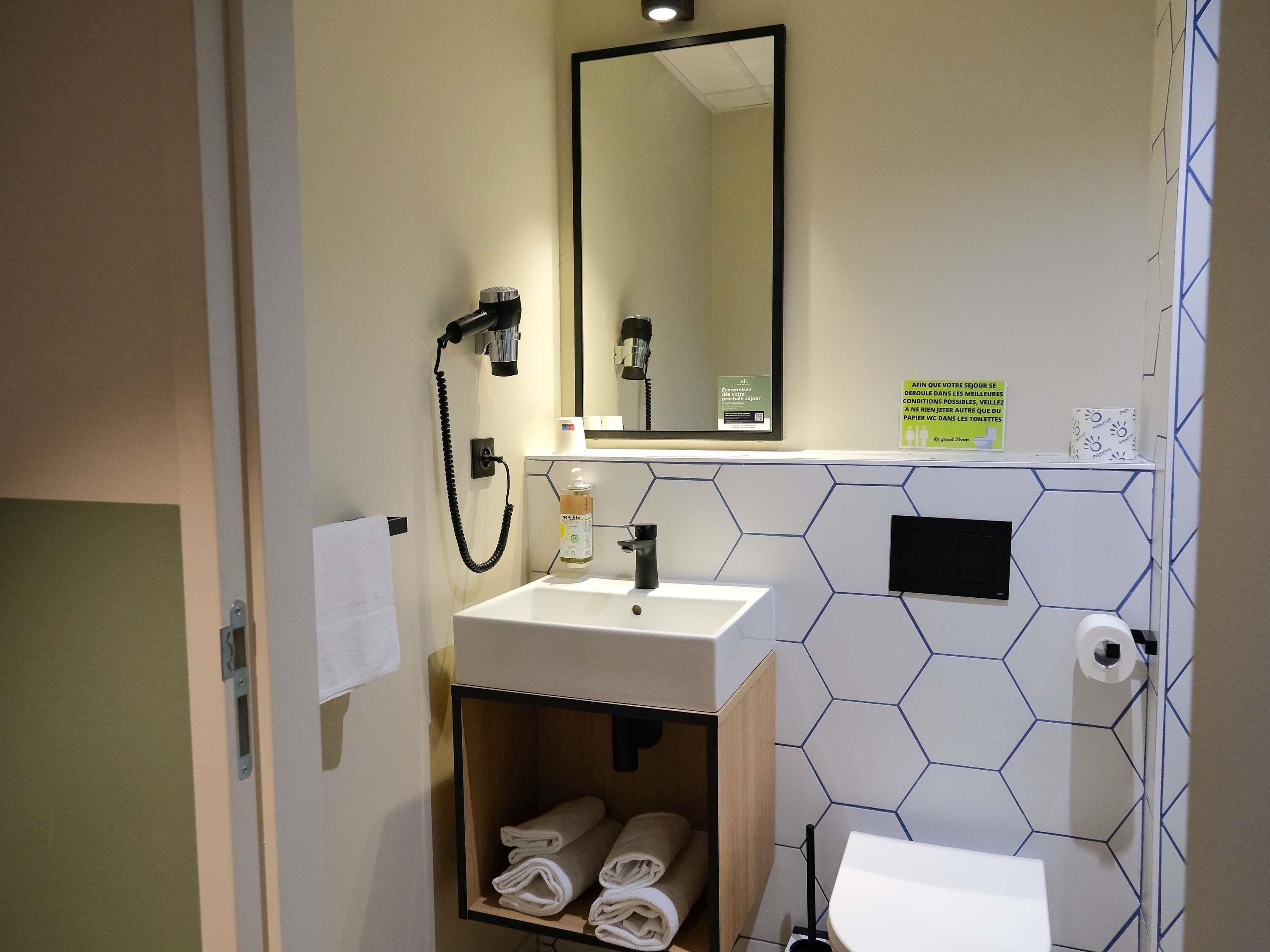Een badkamer met een wastafel, spiegel, handdoekhouder en een wand met een honingraatpatroon.
