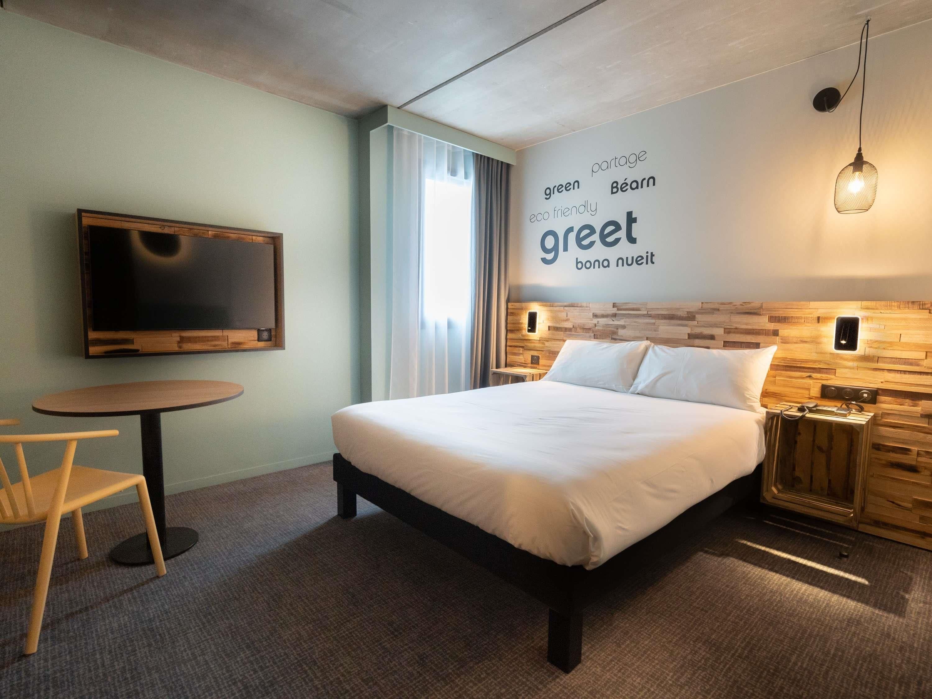 A hotel room with a bed, a TV, a round table, and a wall with eco-friendly text.