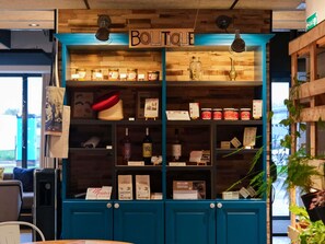 Una tienda boutique con estantes de madera que exhiben diversos productos, un cartel que dice 'BOUTIQUE' y una puerta azul.