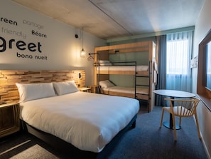Een hotelkamer met een stapelbed, een enkele bed, een kleine tafel en een stoel.