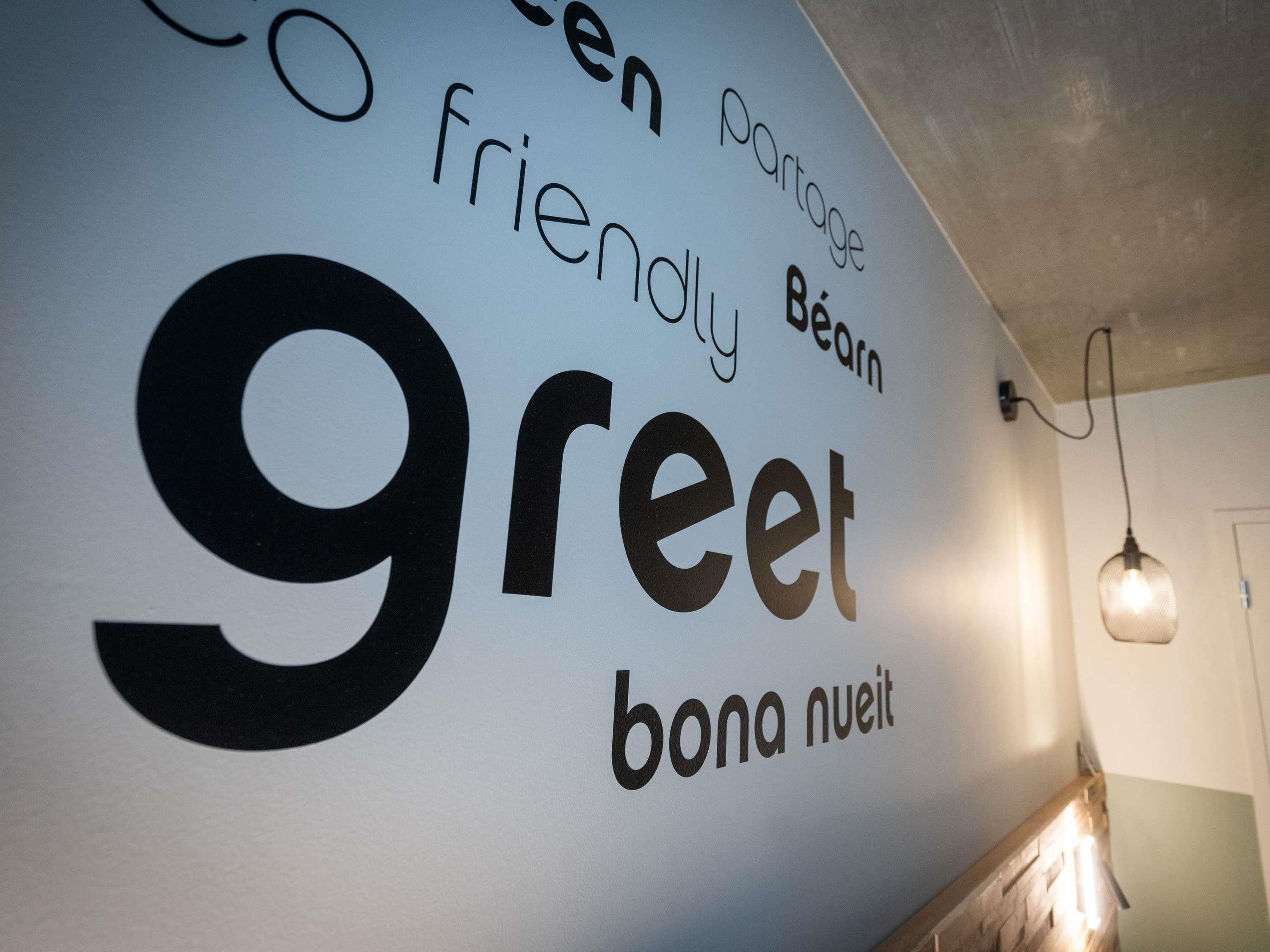 Uma parede com texto em vários idiomas, incluindo 'greet' e 'bona nuit'.