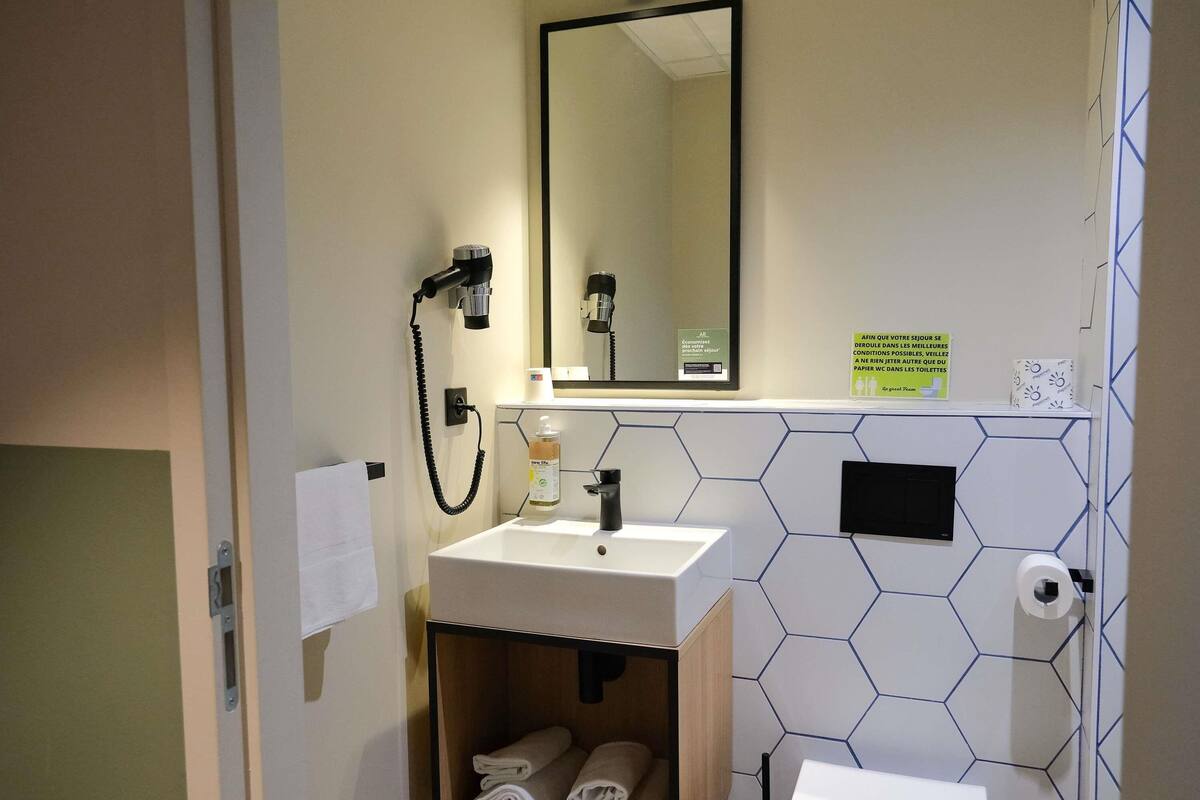 Une salle de bain avec un lavabo, un miroir, un porte-serviettes et un mur recouvert de carreaux hexagonaux.