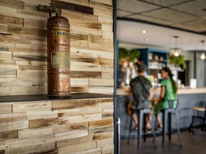 Un extintor de cobre montado en una pared de madera, con una zona de bar al fondo.